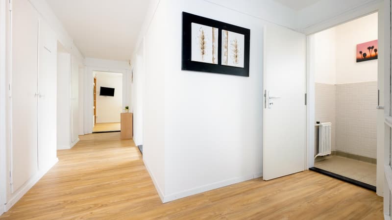 wooden floor, white walls, hallway, picture frame, open door, small plant, mounted TV