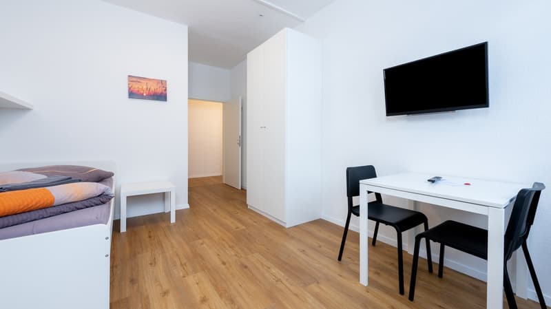 a bedroom with a bed, desk with 2 chairs, mounted television, closet