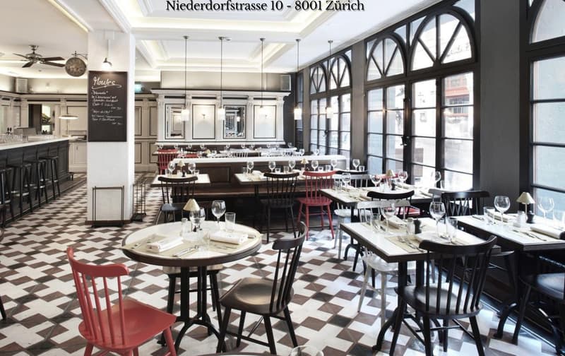 An indoor restaurant with arched windows, checkered floor, wooden tables, high back chairs, a central island, and an open kitchen area.