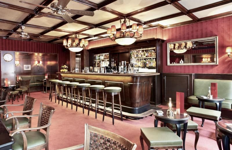 wooden bar counter, stools, wooden tables, red wall, chandelier, seating area, mirror, red carpet, ceiling fan
