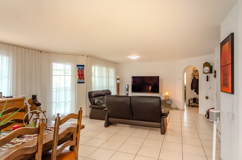 white tiles, two couches, tv on wall, dining table with chairs, painting on wall, clock