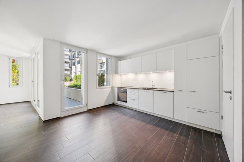 wooden floors, modern white kitchen with modern appliances, two sliding doors leading to a balcony