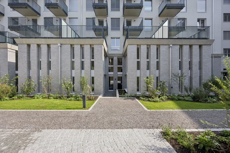 modern apartment building, balconies on each floor, brick exterior, landscaped entrance