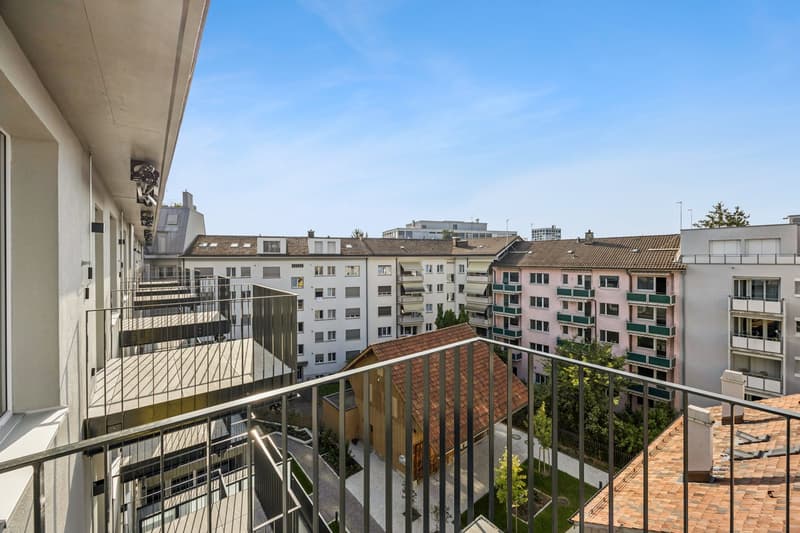 modern building with multiple balconies, residential area, green space, other buildings, clear blue sky