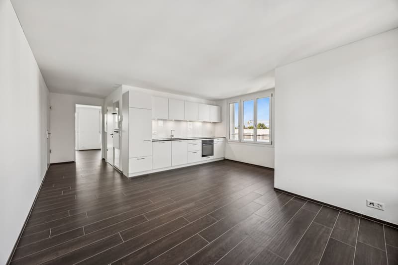 white walls, wooden floor, large window, white kitchen cabinets, kitchen sink, and faucet