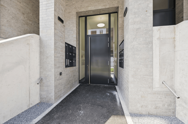 Main entrance to the building, black door, concrete walkway, mailbox, glass panel