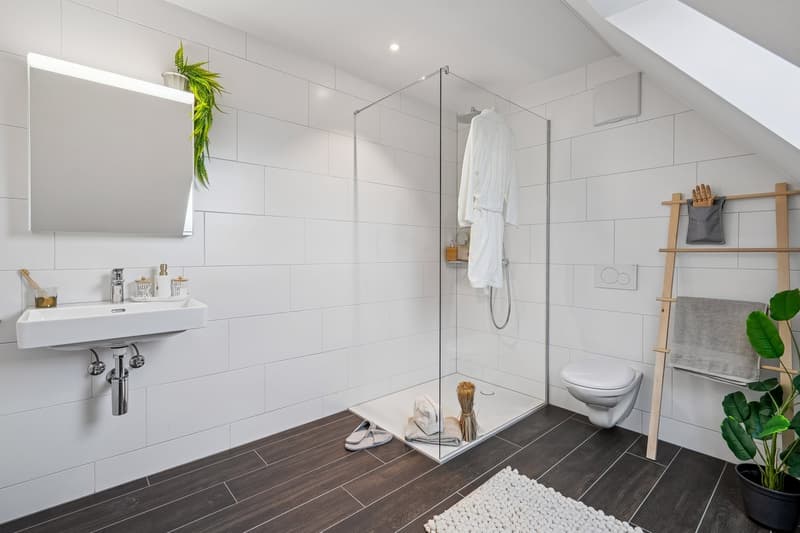 white tiled walls, white floor, modern shower enclosure, white sink, potted plant, towels, mirror above the sink