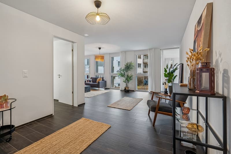modern and minimalist hallway with wooden flooring, neutral walls, floor lamps, rugs, wooden chair, side table, plants, decorative elements, open to living area with couch, windows