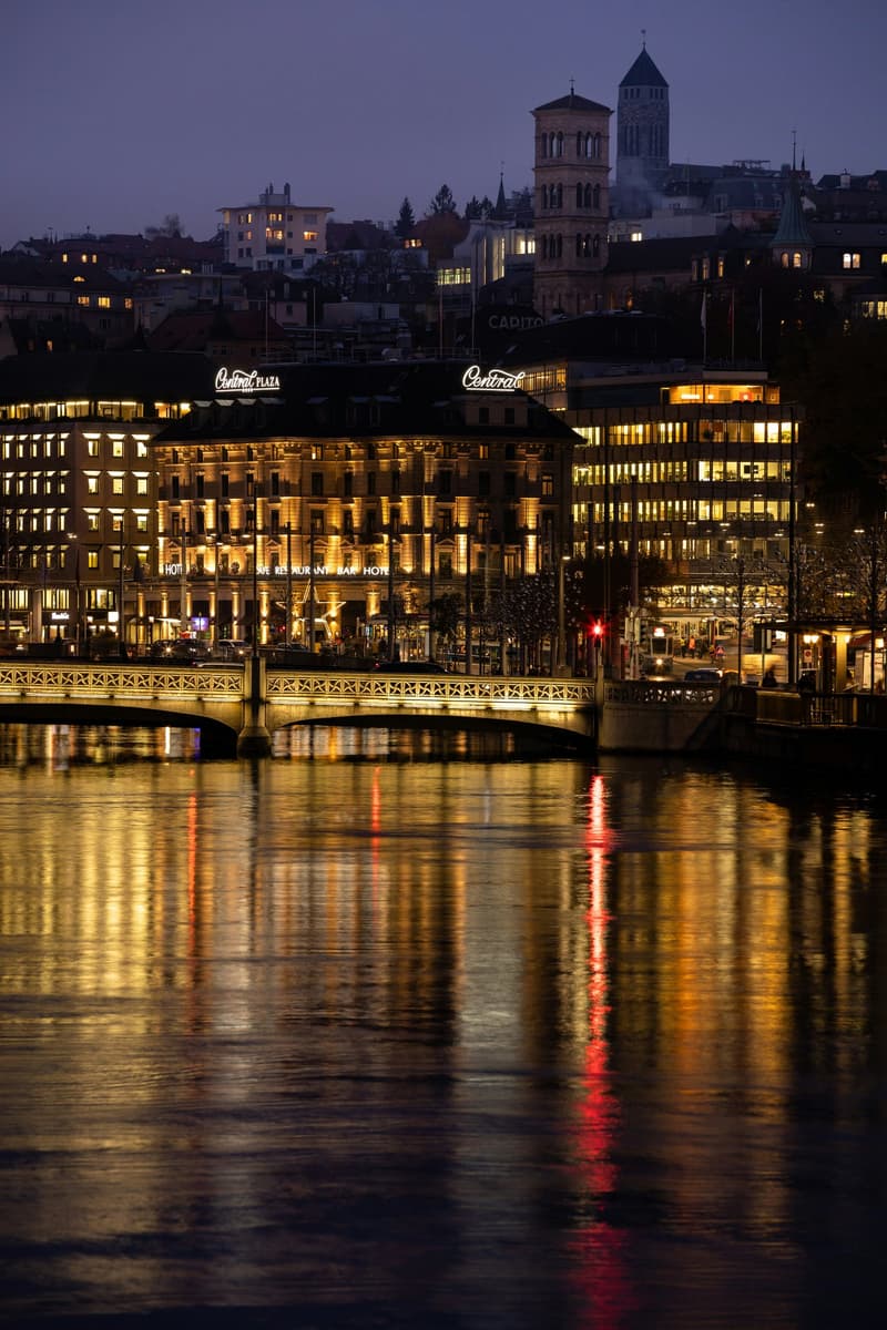 Illuminated cityscape at night, featuring large hotels, historical buildings, and a bridge over a river.