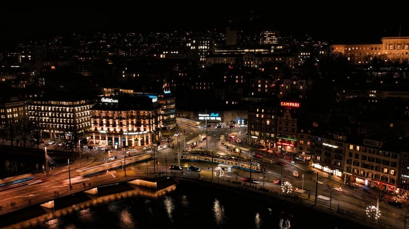 City view with illuminated buildings, busy streets, a river, and a bridge