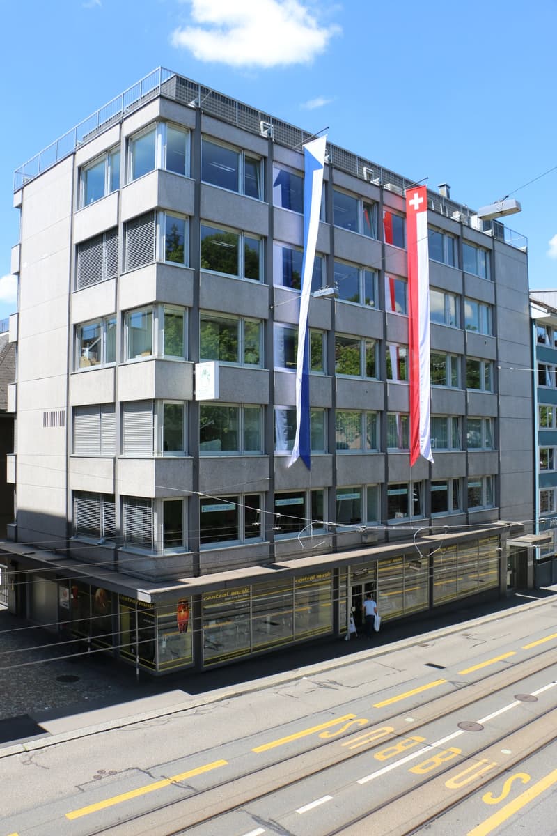 gray concrete exterior, large windows, three flags on building