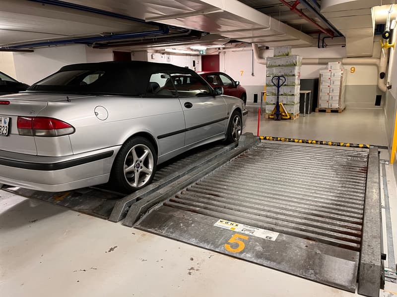underground parking with electric car ramps, gray cars parked, red car in background