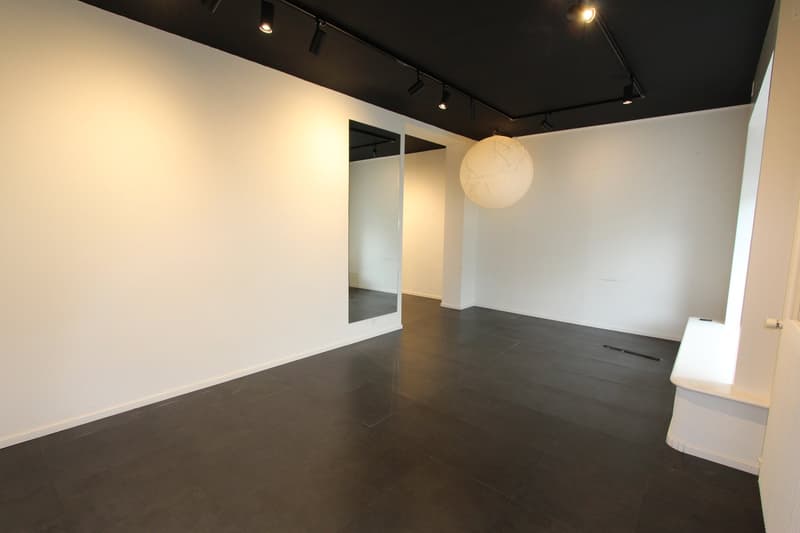 Empty room with white walls, black tiled floor, large mirror, and ceiling lights