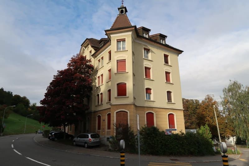 3 story building, beige exterior, red shutters, tower, cars parked in front