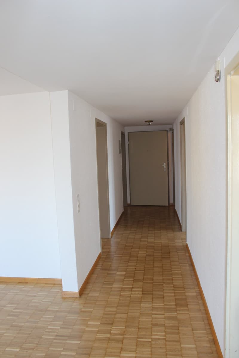 Empty hallway with wooden floors, white walls, and doors on both sides.