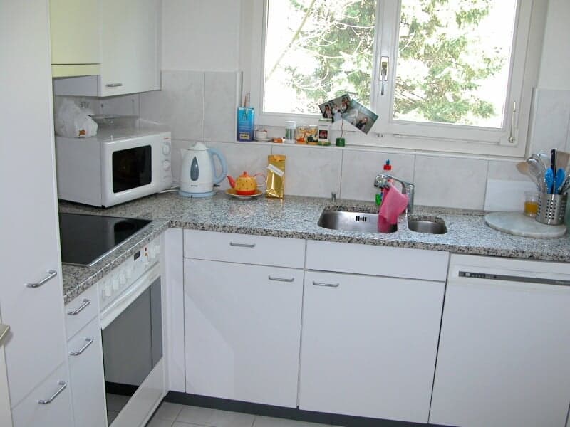 White cabinets, granite countertops, a microwave, an electric kettle, a stove, an oven, a sink, a dishwasher, and a window.