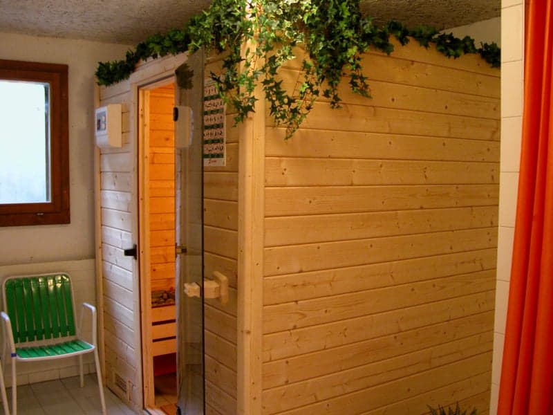 wood paneled sauna room with glass door, green chair, brown window frame, white walls
