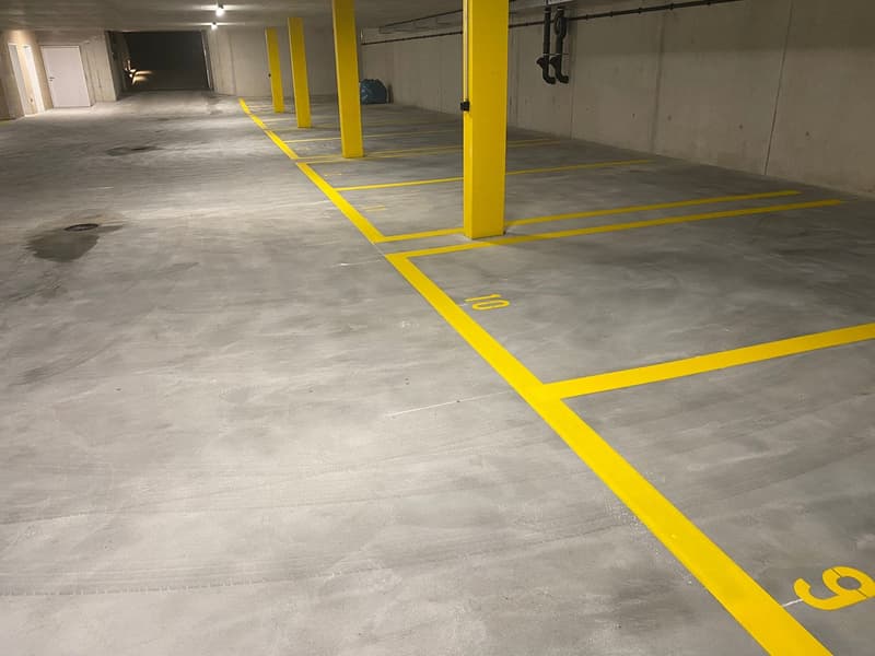 Concrete floor with yellow parking space markings, concrete walls, and yellow support columns.