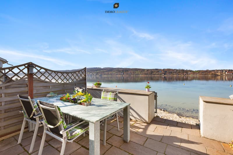Die Seesicht von hier aus ist ein tägliches Geschenk. / a table and chairs on a patio overlooking a lake