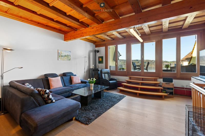 ,,Ein Wohnzimmer, das mit seiner warmen Holzdecke und dem knisternden Schwedenofen Geborgenheit ausstrahlt - gekrönt von einer beeindruckenden Raumhöhe, die Freiheit und Weite schenkt. / a living