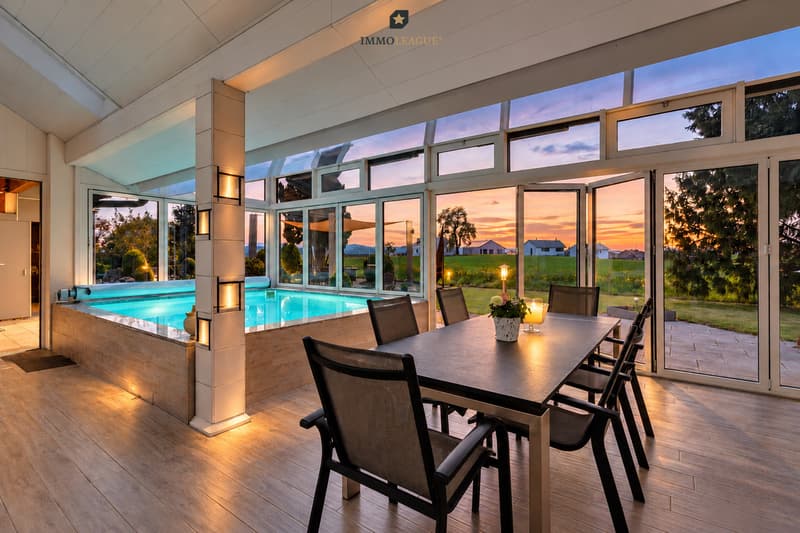 Lichtdurchfluteter Wintergarten mit Indoor-Pool und traumhaftem Blick auf den Sonnenuntergang.