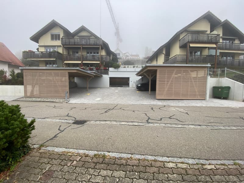 Apartment building with carport, driveway, two garages with closed doors, and two covered parking spaces.