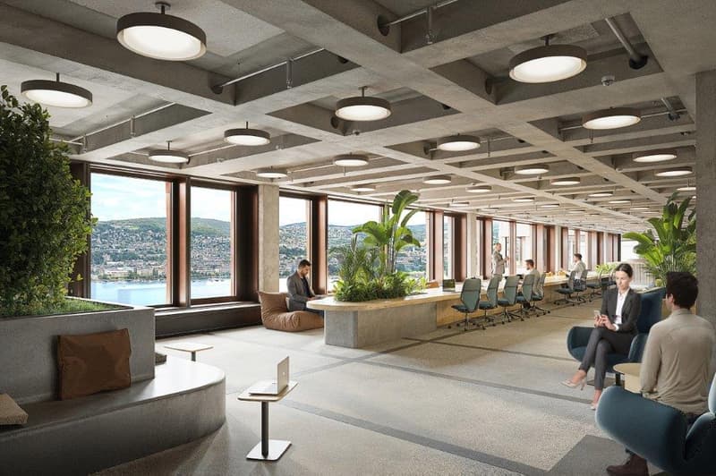 large room with office chairs and desks, plants, concrete ceiling with multiple lights, windows with a city view