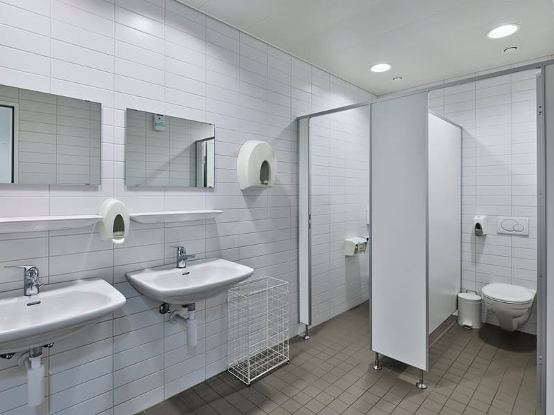 Large bathroom with white tile walls, two sinks, mirrors, toilet, and a stall shower area