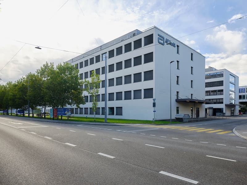 A multi-story office building with a modern, gray exterior and large windows. The building has multiple floors and appears to be located on a street with multiple lanes of traffic and pedestrian walkways.