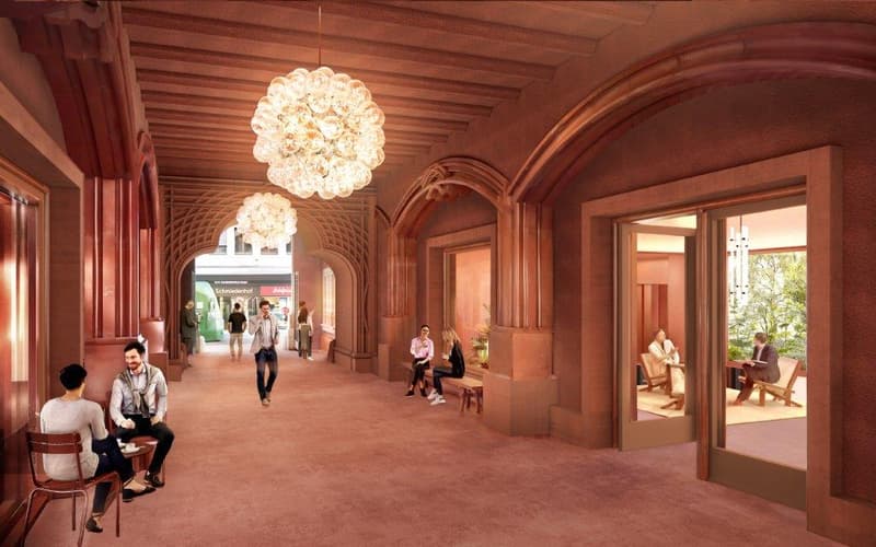 Large indoor space with arched doorways, wooden beams on the ceiling, and a large chandelier. Several people are seated and walking through the hallway.