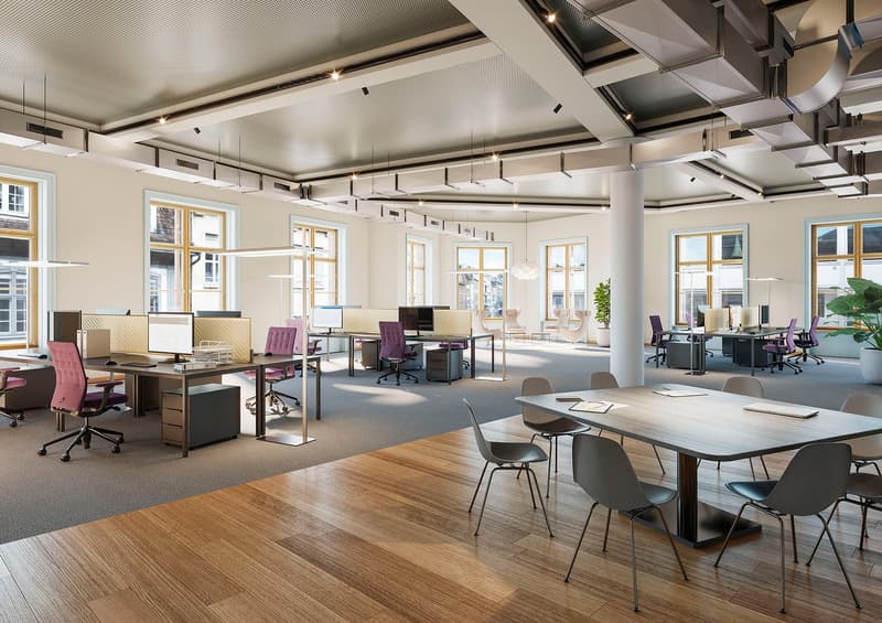 Large open-plan office space with high ceilings, large windows, wooden floors, and modern furniture including desks, chairs, and computers. The space has a bright and airy feel with a mix of work and collaborative areas.
