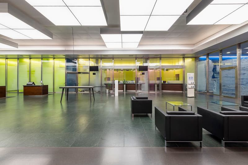 Large open office lobby with modern design, green and yellow glass partitions, reception desk, and lounge seating area