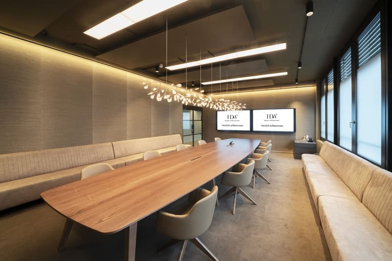 wooden table, chairs, white walls, carpets, two sofas, two monitors with messages