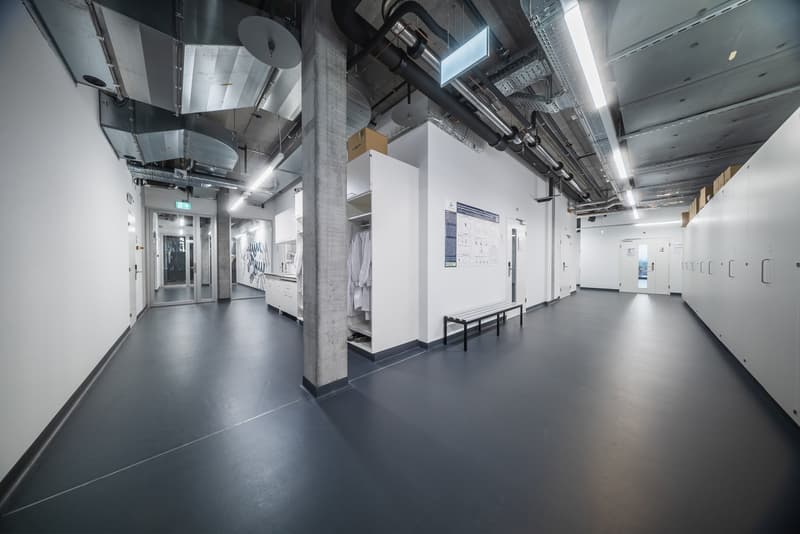 large hallway, white walls, ceiling lights, metal beams, lockers, black floor