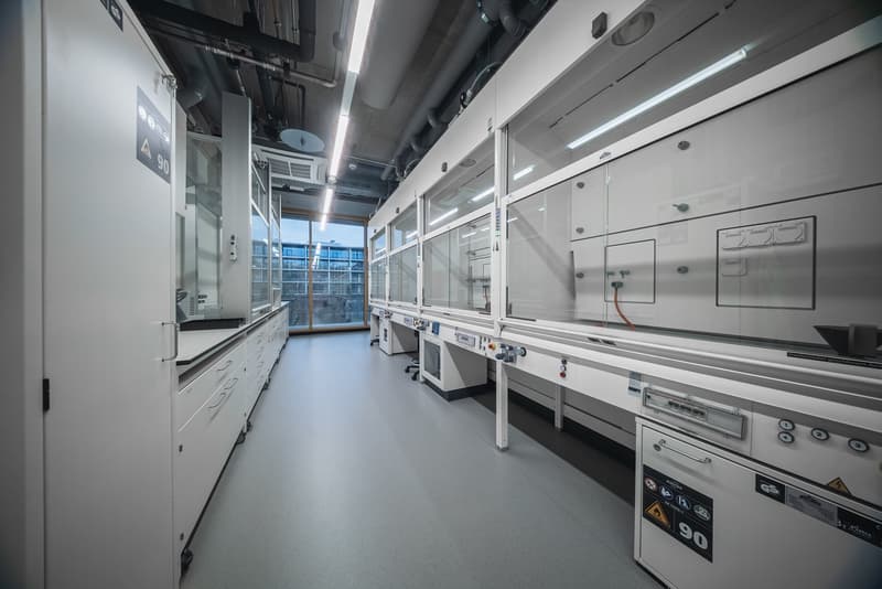 Clean laboratory room with white walls, ceiling with mounted lighting, multiple white cabinets, glass panels, and electrical switches.