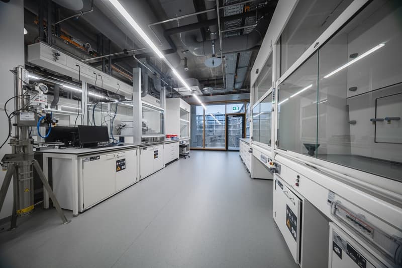 Lab area with white cabinets, counters, industrial machines, large windows, gray floor.