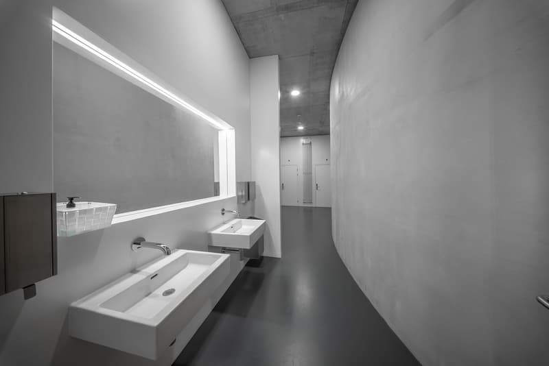 Modern bathroom with 2 sinks, white walls, curved wall, stainless steel faucets, soap dispensers, mirror, bright lighting, black floor
