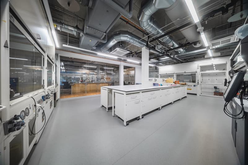 spacious room with white cabinets, a large central desk, glass walls, modern equipment, gray floors, metal pipes