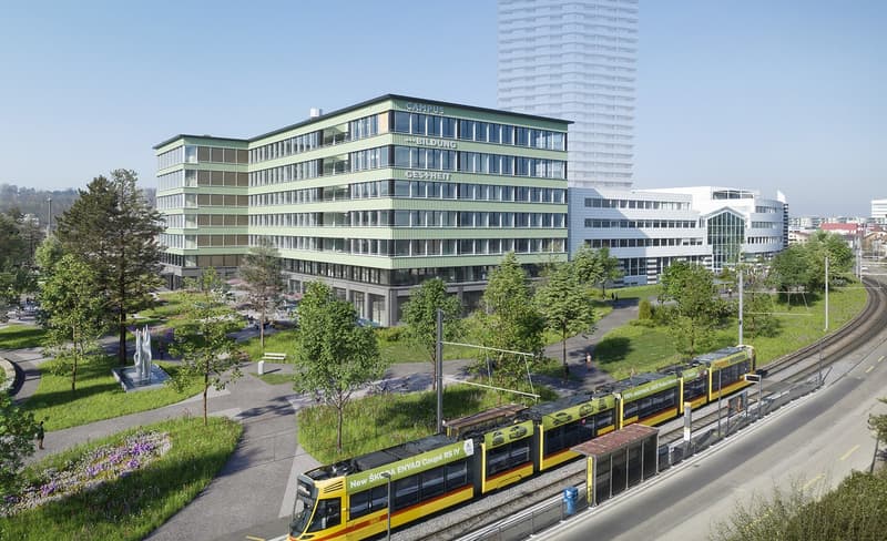 Office building with multiple floors, green facade, large windows, adjacent to a tram track, surrounded by trees and grass