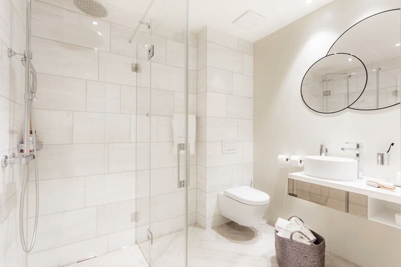 white tiles, modern design, glass shower enclosure, white porcelain sink, white toilet, modern faucets, mirrors, toilet paper holder, toiletries