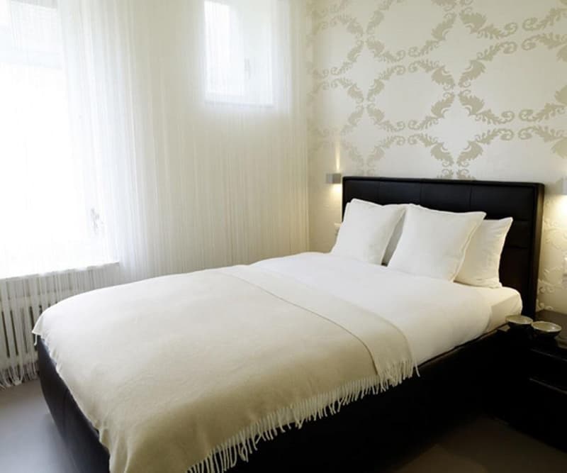spacious bedroom with double bed, white linens, white curtains, patterned wall, white walls, large window