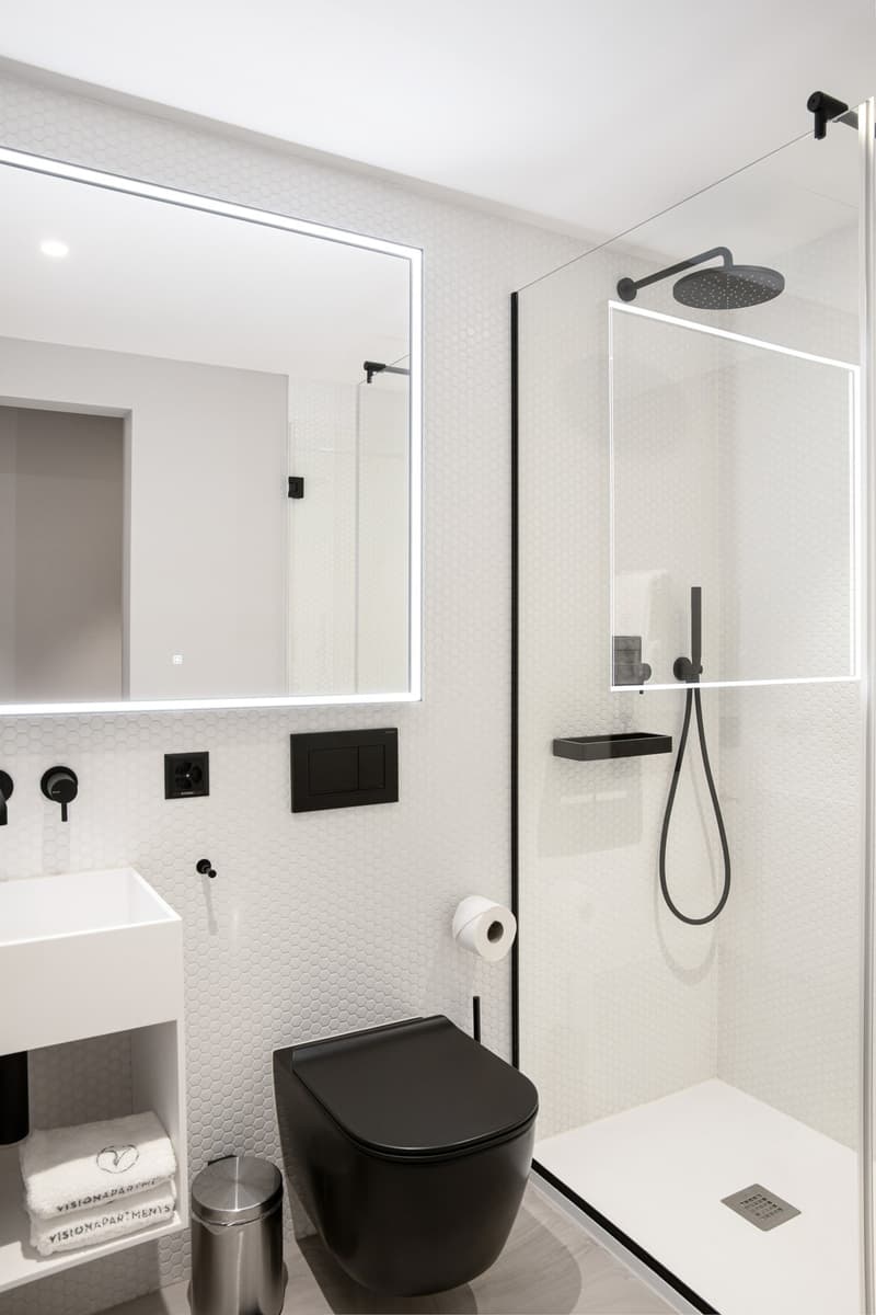 modern minimalist bathroom, glass shower stall, black toilet, white hexagon tile, mirror with LED strip