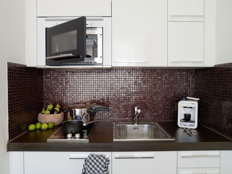 modern kitchen, white cabinets, brown tiled backsplash, stainless steel sink, gas stove, microwave, coffee machine, black countertop