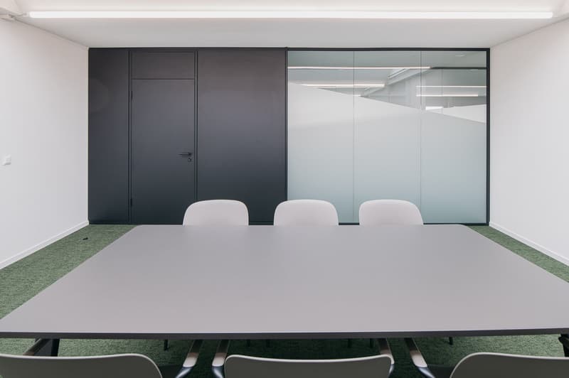 modern office room with a rectangular table, chairs, a glass wall, a gray wall, and a glass door