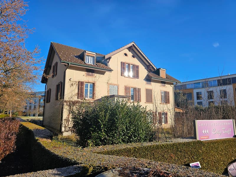 2 story house, brown roof, beige walls, multiple windows, surrounded by bushes and trees, sign for cafe restaurant