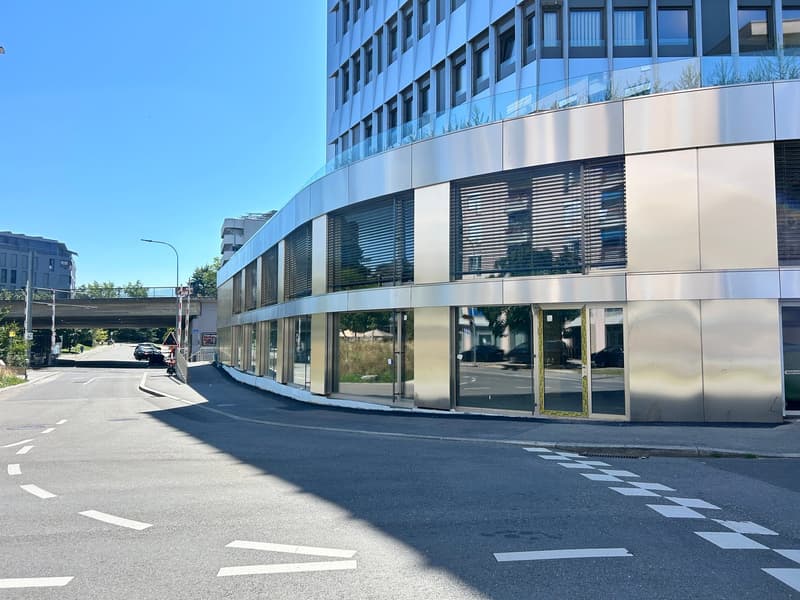 This image shows a modern, multi-story office building with a curved glass facade and a ground floor with large windows. The building has a sleek, contemporary design with a mix of glass and metal materials. The surrounding area appears to be a city stree