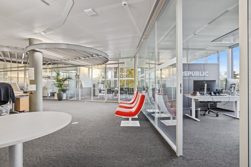 spacious office with glass walls, modern furniture, red chairs, round table, grey carpet