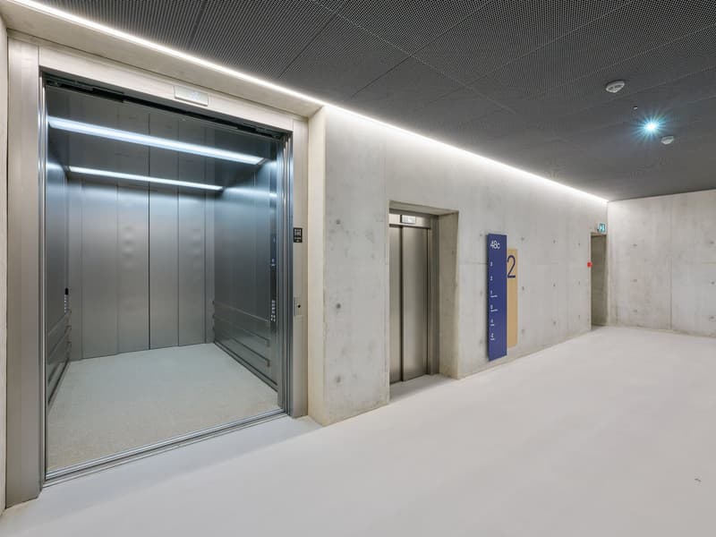 elevator, concrete walls, metal ceiling, large open space, light panels, two elevator shafts