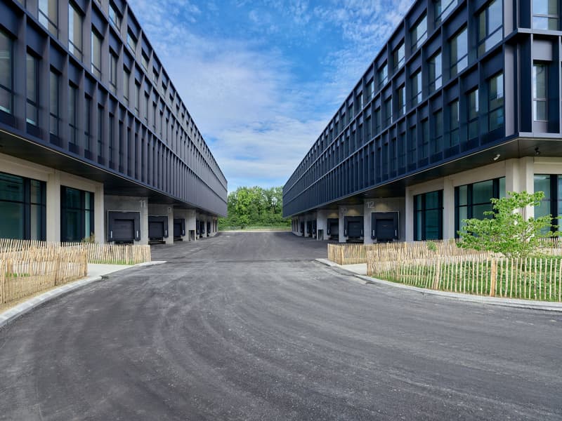 Modern office buildings with windows, two black garages, wide road between buildings, fences on both sides.