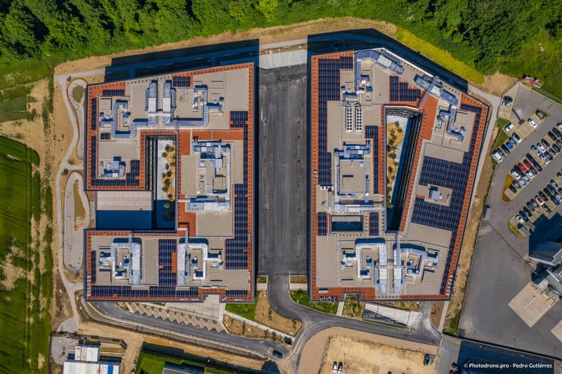 Two buildings connected, solar panels, parking area with many cars
